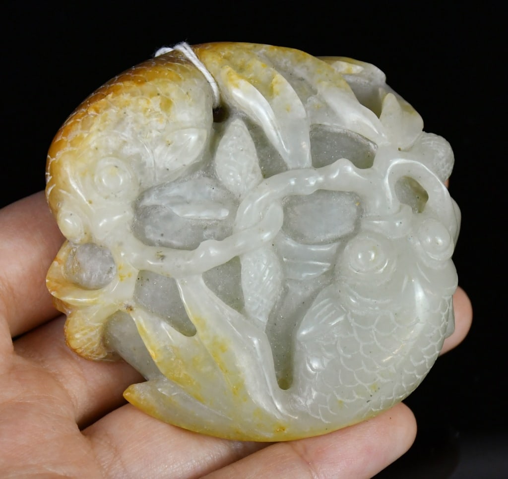 A Jade Carved Double-Fish Ornament Republican: The white jade carving worked in the form of two fish amidst lotus leaves, the pale celadon stone with russet inclusions. 6.8x6.7cm 民國 玉雕雙魚荷葉