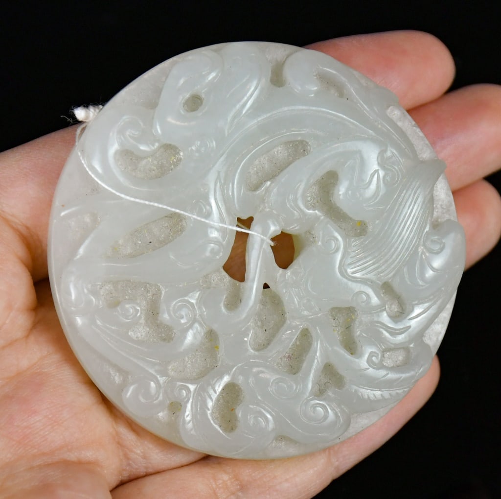 A White Jade Carved Chilong Bi Disc Qing: The circular white jade bi disc carved in relief with a chilong amidst scrolling cloud motifs, the reverse decorated with raised bosses, the stone of pale celadon-white tone. D: 5.7cm 清 白