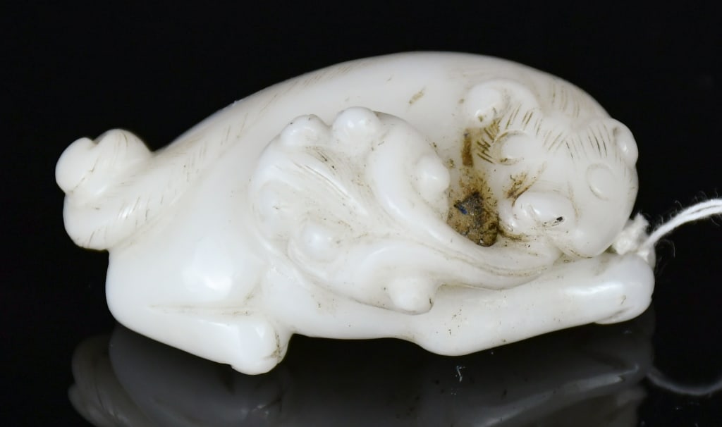 A White Jade Carved Beast Republican: Carved as a recumbent mythical beast grasping a lingzhi spray in its mouth, the stone of white tone. 5.8x4.1cm 民國 白玉雕瑞獸把件