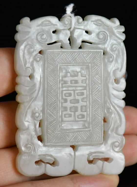 A Celadon Jade Carved Plaque Qing: The rectangular jade plaque carved with a central geometric panel enclosing a Chinese character, surrounded by openwork dragon motifs, the stone of pale celadon even tone. 6x4.2cm 清 青