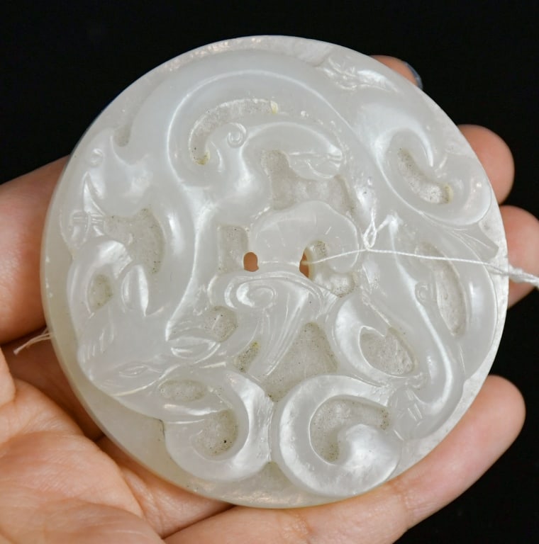 A White Jade Carved Chilong Bi Disc Qing: The circular white jade bi disc carved in relief with a chilong amidst scrolling cloud motifs, the reverse decorated with raised bosses, the stone of pale celadon-white tone. D: 6cm 清 白&
