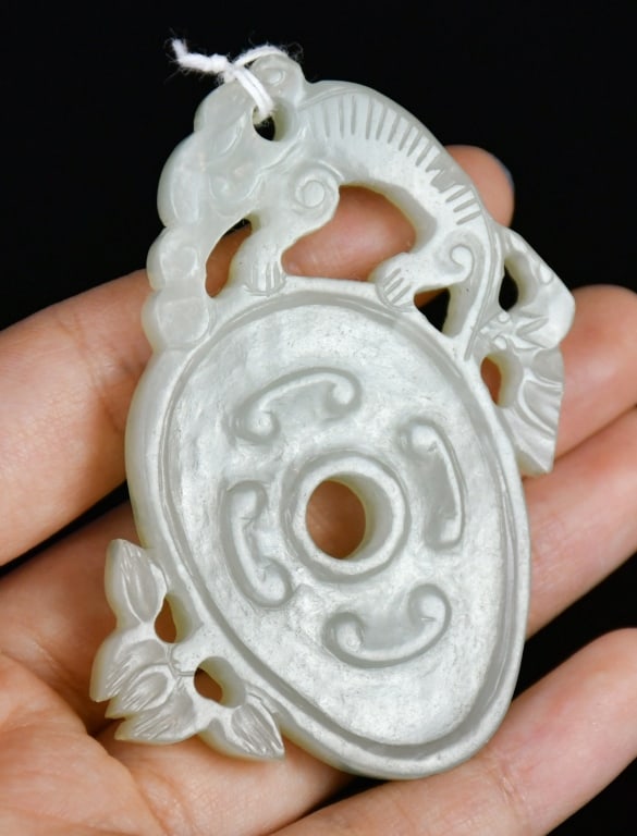 A Celadon Jade Openwork Disc Qing: The oval white jade bi disc surmounted by a chilong and flanked by foliate motifs, the stone of pale celadon even tone. 4.3x6.7cm 清 青玉雕螭龍紋出ò