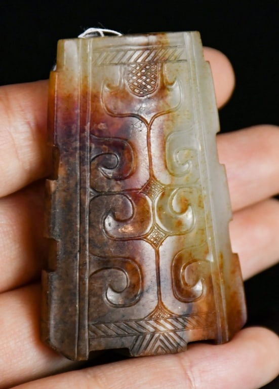 An Archaistic Beige Jade Scabbard Slide: Of trapezoidal form, the stone of celadon tone with russet inclusions, both sides are carved in low relief with archaistic scroll motifs. 5.8x3.6cm 高古風格 刻紋