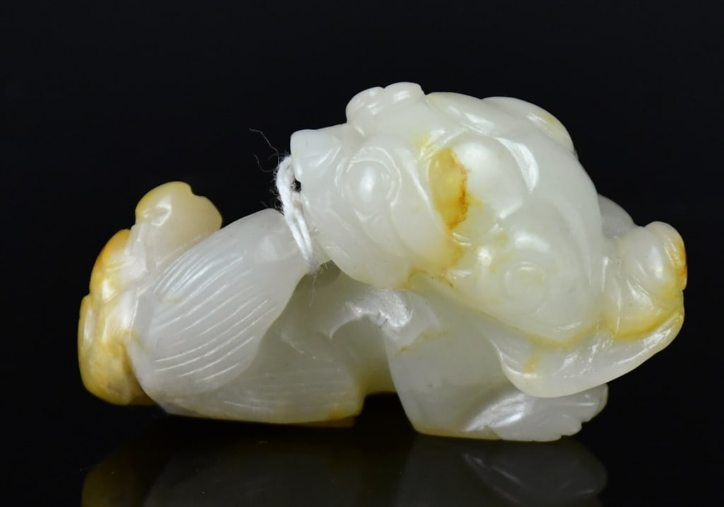 A Celadon Jade Carved Beast Qing: Carved as a mythical beast turning its head back to bite its tail, the stone overall of pale celadon tone. 5.3x4.1cm 清 青玉雕瑞獸把件
