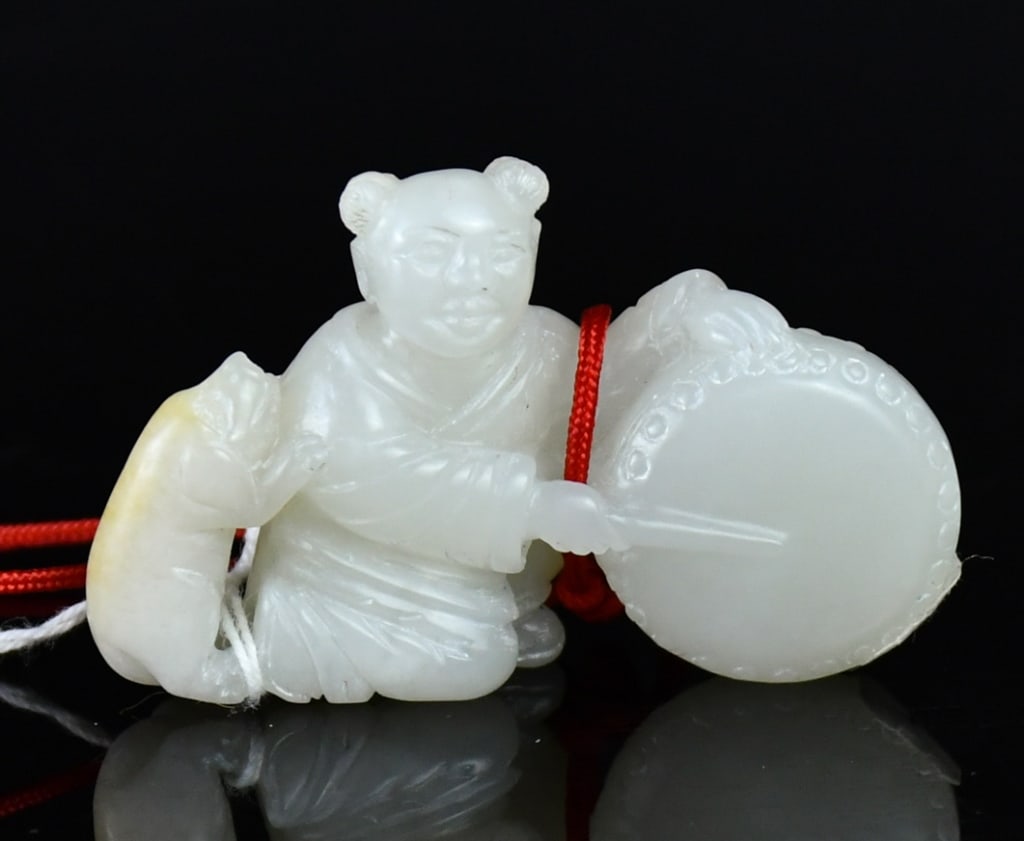 A White Jade Carved Figure Qing: Carved as a child holding a drum and drumstick beside a small pig, the stone of even white tone. 5x3.1cm 清 白玉雕童子擊鼓擺件