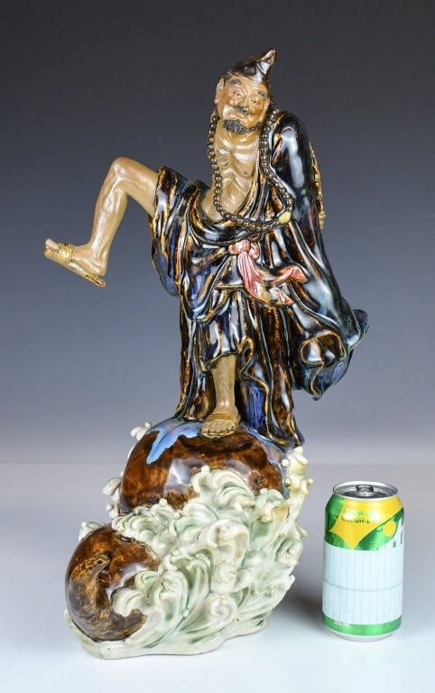 Wu JuQiang (1951-) A Shiwan Porcelain Figure: Modeled as Ji Gong standing atop a double-gourd-form base surrounded by cresting waves, marked on the figure with the maker's seal. H: 47.8cm 吴鉅强 (1951-) 石灣人&
