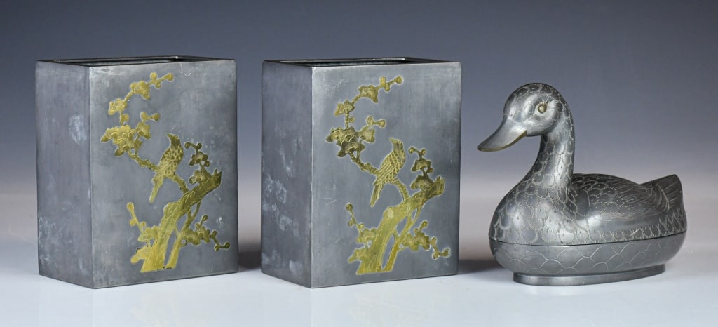 A Group of 3 Pewter Articles Republican: Comprising a pair of square-section pots, each decorated with a bird perched on a flowering branch, together with a duck-form model, the surface finely engraved with feathers. Largest H: 17.8cm. Each 