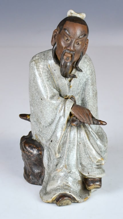 A Shiwan Kiln Figurine w/Mk 19thC: The figure is finely modeled, seated in a relaxed posture upon an integral rocky base. He is depicted wearing a voluminous, pale-celadon glazed robe characterized by a fine crackle pattern, gathered a