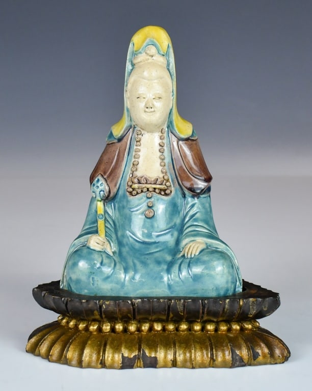 A Fahua-glazed Figure of Guanyin Qing: Modelled seated in dhyanasana on a separately wood-carved gilded lotus pedestal. The figure is clad in long, flowing robes glazed in a rich turquoise hue, under a brown-glazed capelet and a vibrant ye
