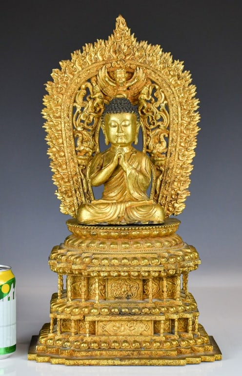 A Sino-Tibetan Gilt-Bronze Seated Buddha 18-19thC: The deity is heavily cast and depicted seated in padmasana on a lotus throne, with hands held together at the chest in a variation of anjali or uttarabodhi mudra. The figure is backed by an elaboratel