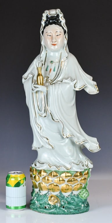 A Lrg Parcel-Gilt Famille Rose Guanyin Republican: Bodhisattva of Compassion is depicted standing atop an integrated lotus throne rising from swirling turquoise-enamelled waves. She wears long robes with detailed folds highlighted in gilt borders,