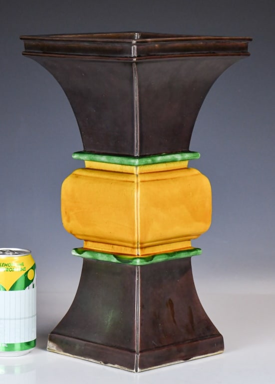 A Sancai-Glazed Archaistic Square Vase Wanli Mk: Modeled after ancient bronze ritual vessels, the square-sectioned body features a flared trumpet neck and a matching spreading foot covered in a deep aubergine-brown glaze. The central bulbous