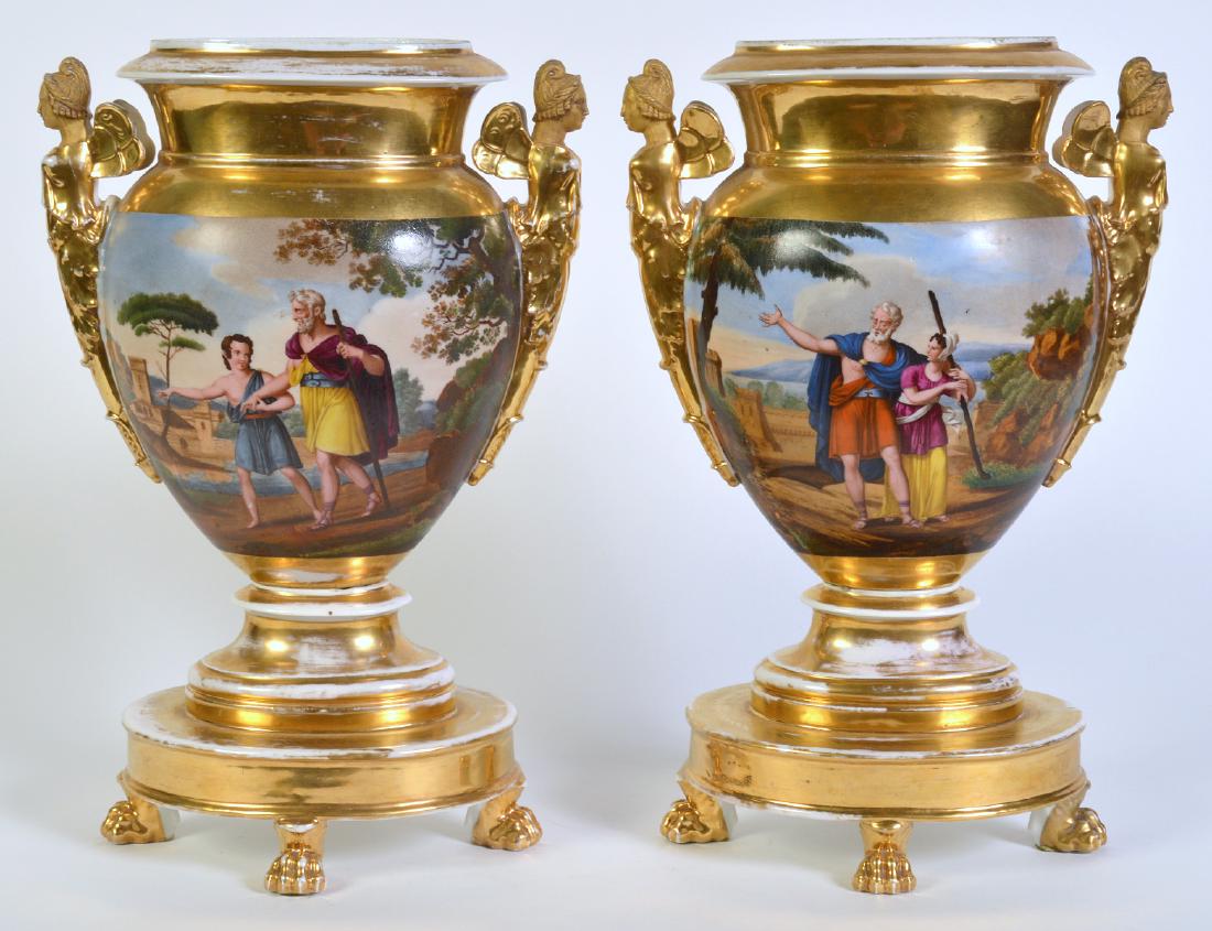 Wonderful Pair Old Paris Footed Urns: Pair of Old Paris gilt urns with oval base, raised on 4 paw feet. Each has 2 painted panels with a figural and a landscape scene surrounded by gilt background and base. Handles on each side are Caryat
