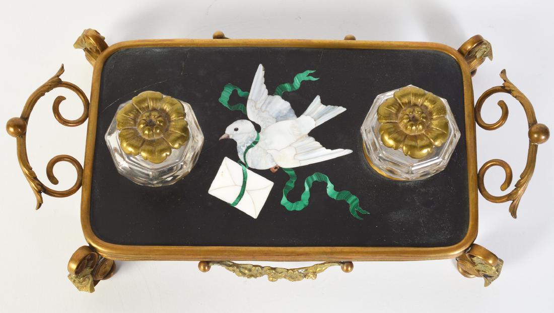 Bronze Mounted Pietra Dura Inkstand: Bronze decorative inkstand with pietra dura top featuring a white dove carrying an envelope on a black background. Tray is raised on 4 scrolled legs with faces, floral swags on sides and curled handle