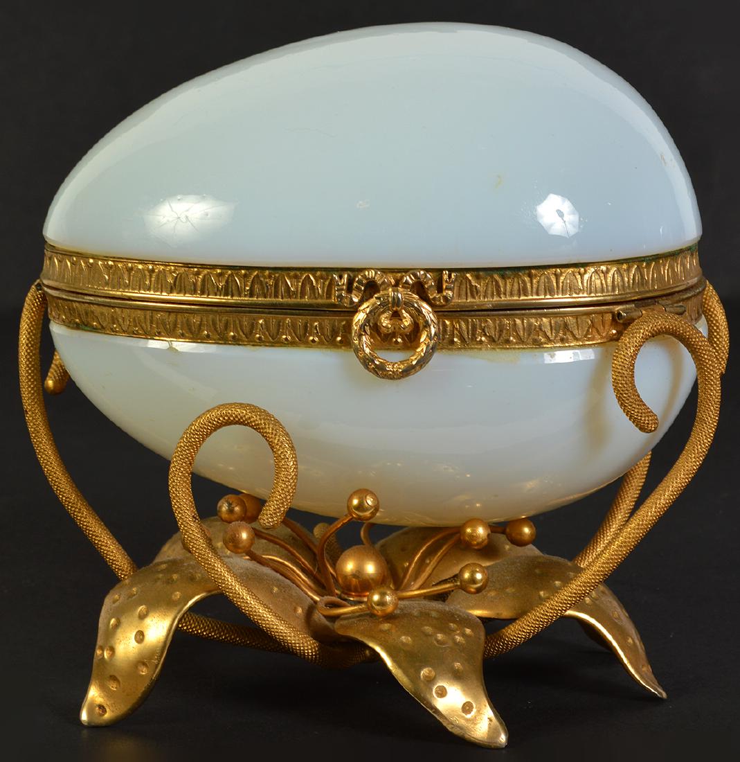 White Opaline Egg on Dore Bronze Base: White opaline egg with dore bronze mounts and flower shaped base. Measures 5"H x 5"L x 4"W. Condition is good with no apparent issues, see photos. Examine all photos closely. Contact AAG for more deta
