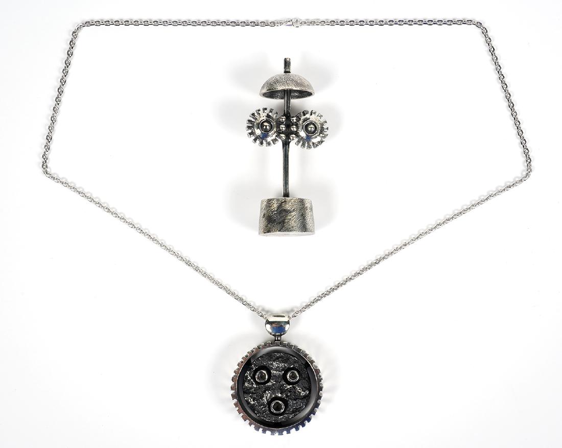 Guy Vidal Sculptural 'Clock' Pendant with Base: Guy Vidal sculptural 'Clock' pendant suspended on 28" chain, comes with base. Round wheel shaped pendant resembles a clock, signed on bottom, comes with stand/base that has cogs/wheels. Measures 6 3/8