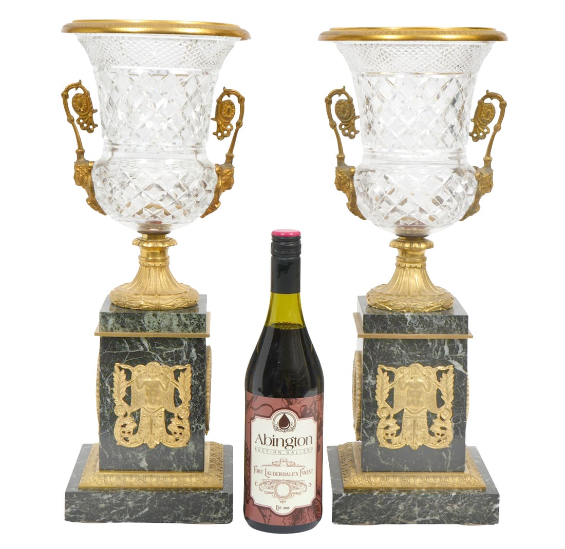 Pr. Bronze Mounted Crystal Urns Marble Bases: Pair of French cut crystal urns with elaborate sculptured ormolu mounts, detailed handles and marble bases. Measures 19.25"H; 7.25"W top; 6.5"x 6.5" marble base. Condition: good condition, please see