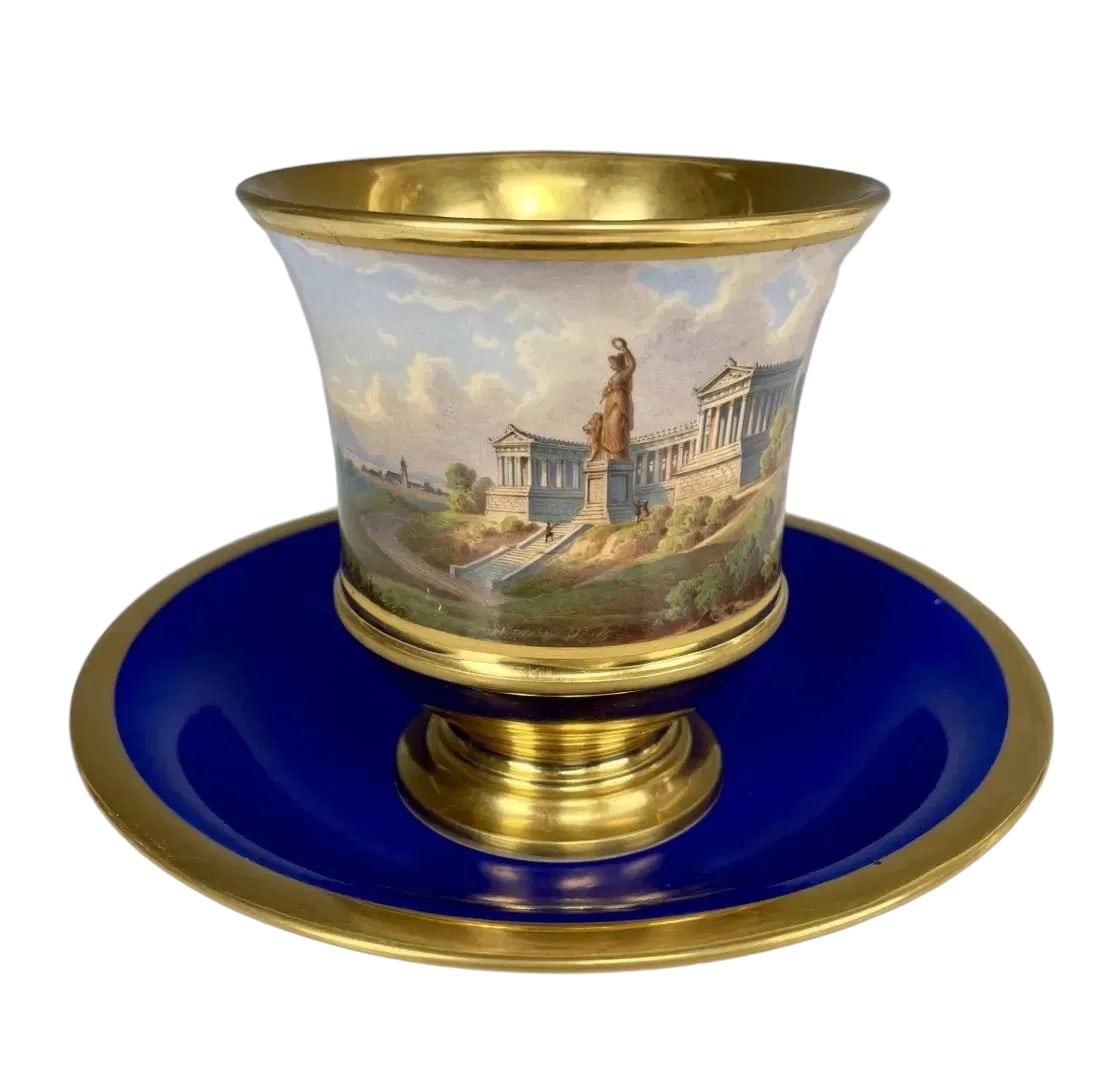 19TH C. NYMPHENBURG TOPOGRAPHICAL CUP AND SAUCER: Stunning finely hand painted decor of the Hall of Fame with the great Statueof Bavaria. This decoration is surrounded by fine gilding with a magnificent blue background. The inside of the cup is also 