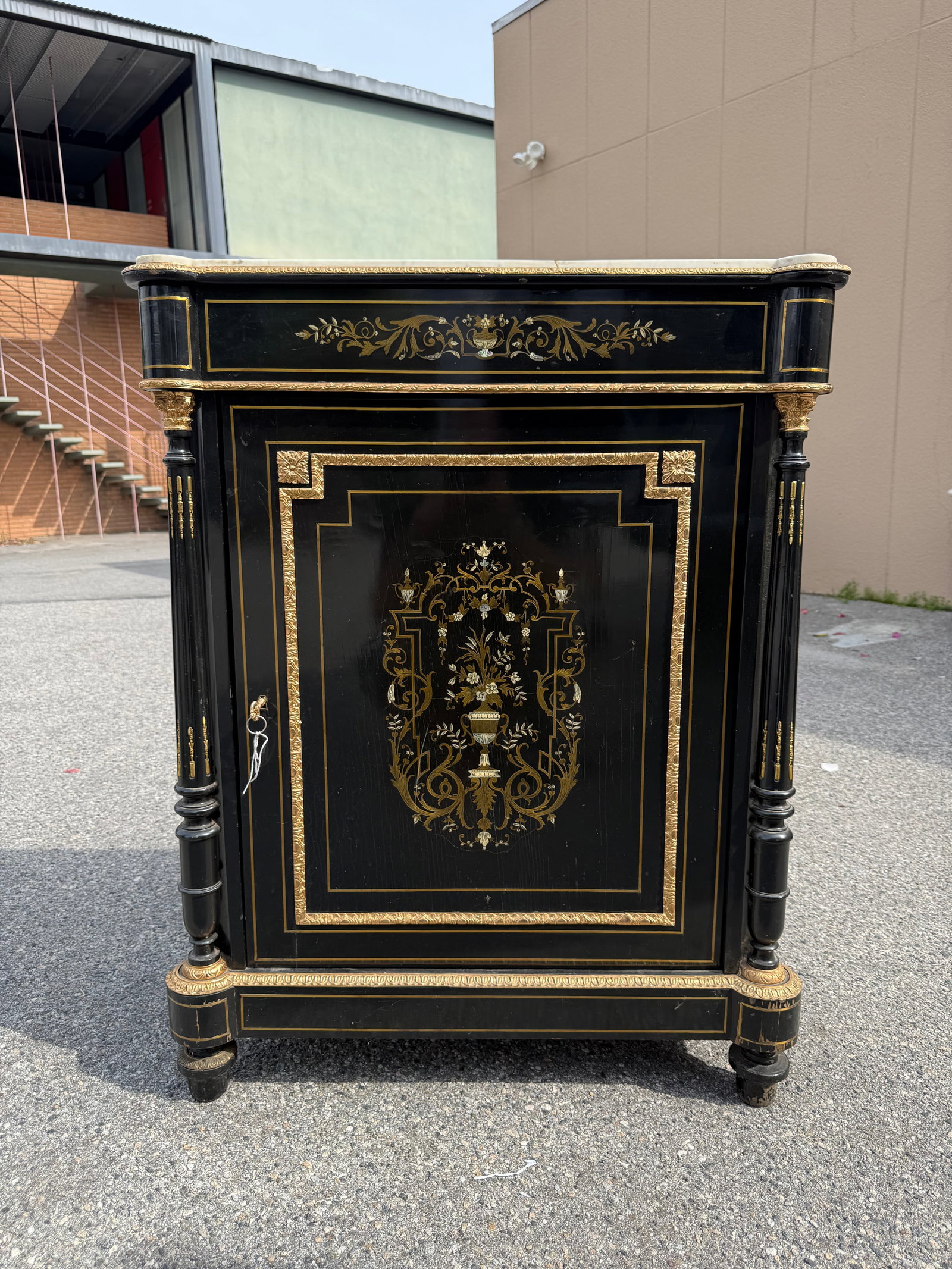 Antique Napoleon III Style Ebonized Cabinet with Marble Top: Elegant ebonized wood cabinet has a white marble top with a visible crack. The front door and top frieze feature intricate brass and mother-of-pearl marquetry in a floral and urn motif. Gilt bronze