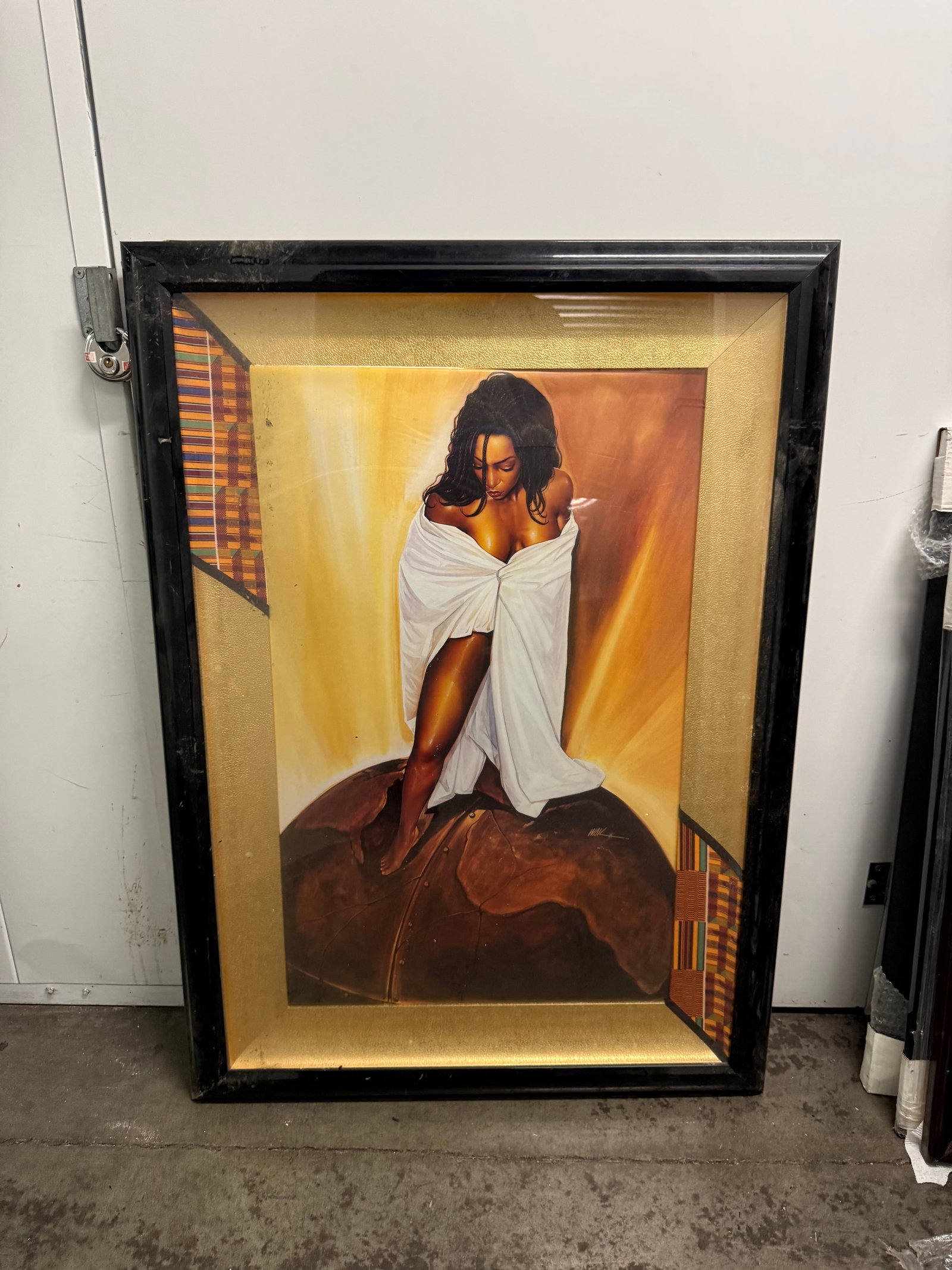 Framed Art Print by Waik - Woman in White Wrap 46”x33”: Large framed art print features a central figure of a woman draped in a white cloth standing on a textured globe. The piece is set within a gold-toned textured mat with colorful geometric patterned ac
