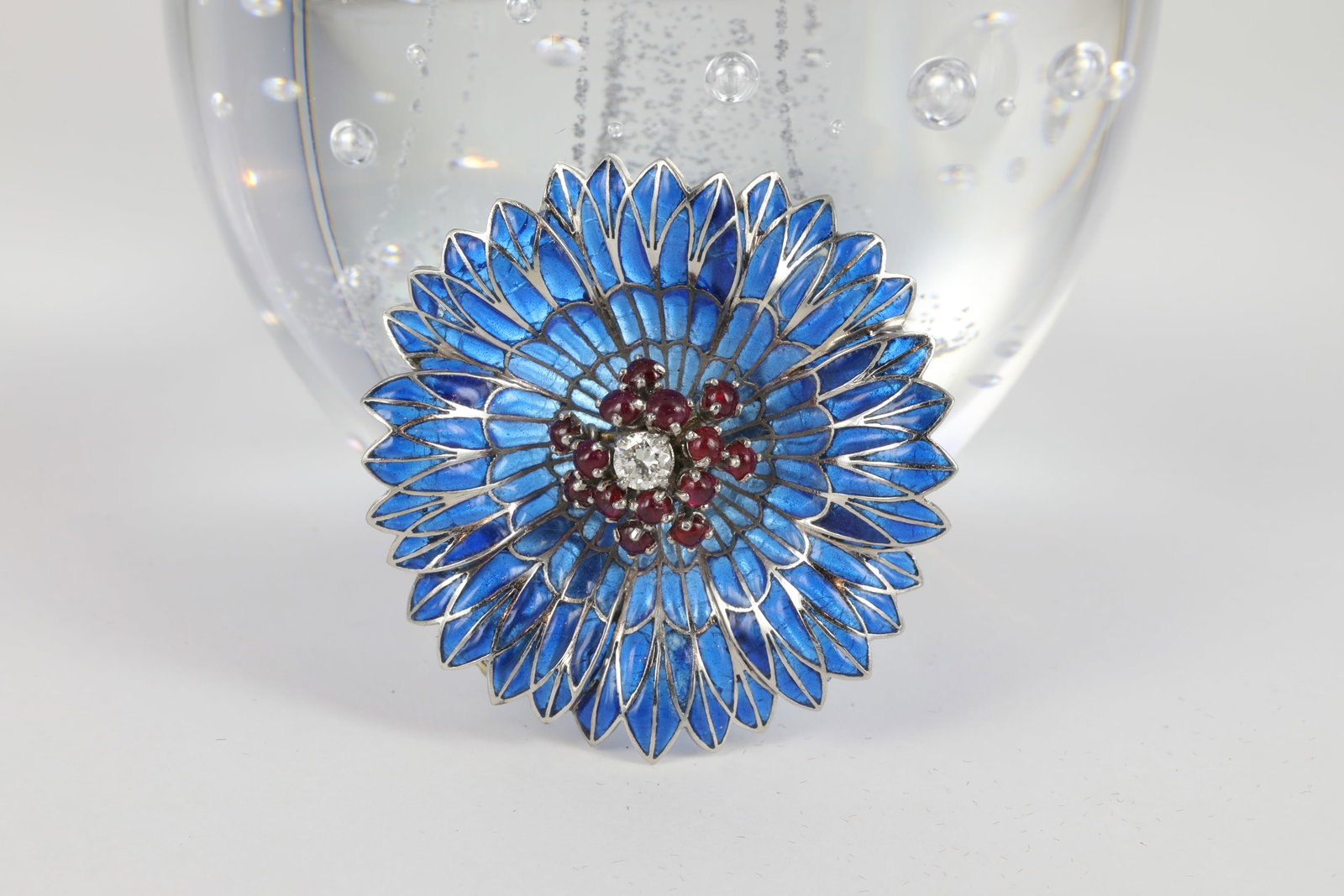 FRENCH PLIQUE-A-JOUR FLOWER BROOCH: Mid 20th century. Designed as a sculpted blue plique-Ã -jour and 18K white gold (tested) flower, central cluster featuring one round diamond, approx. .23ct., surrounded by fourteen round ruby