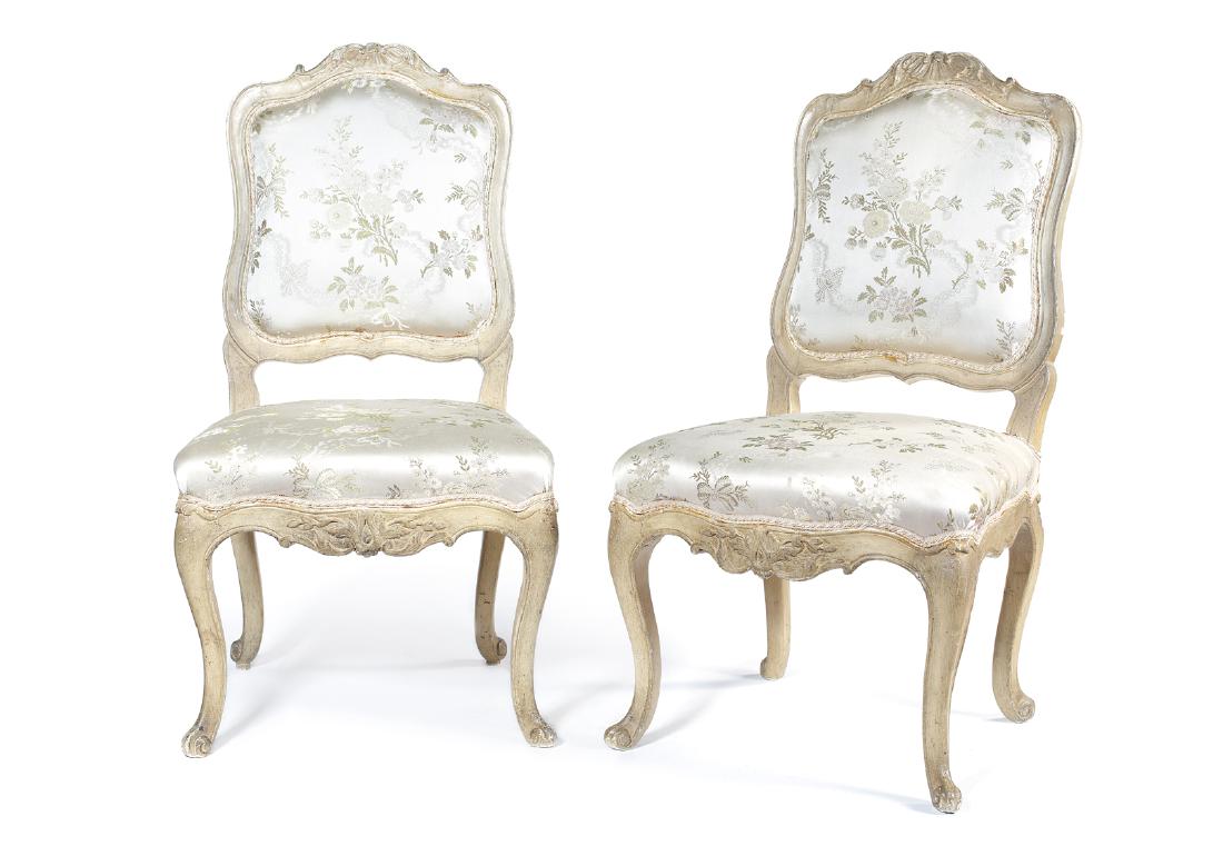 A pair of Louis XV cream painted carved chaises: A pair of Louis XV cream painted carved chaises Upholstered in gold floral silk, the shaped cartouche padded backs with scrolling leaf and shell carved cresting above serpentine seats on cabriole legs