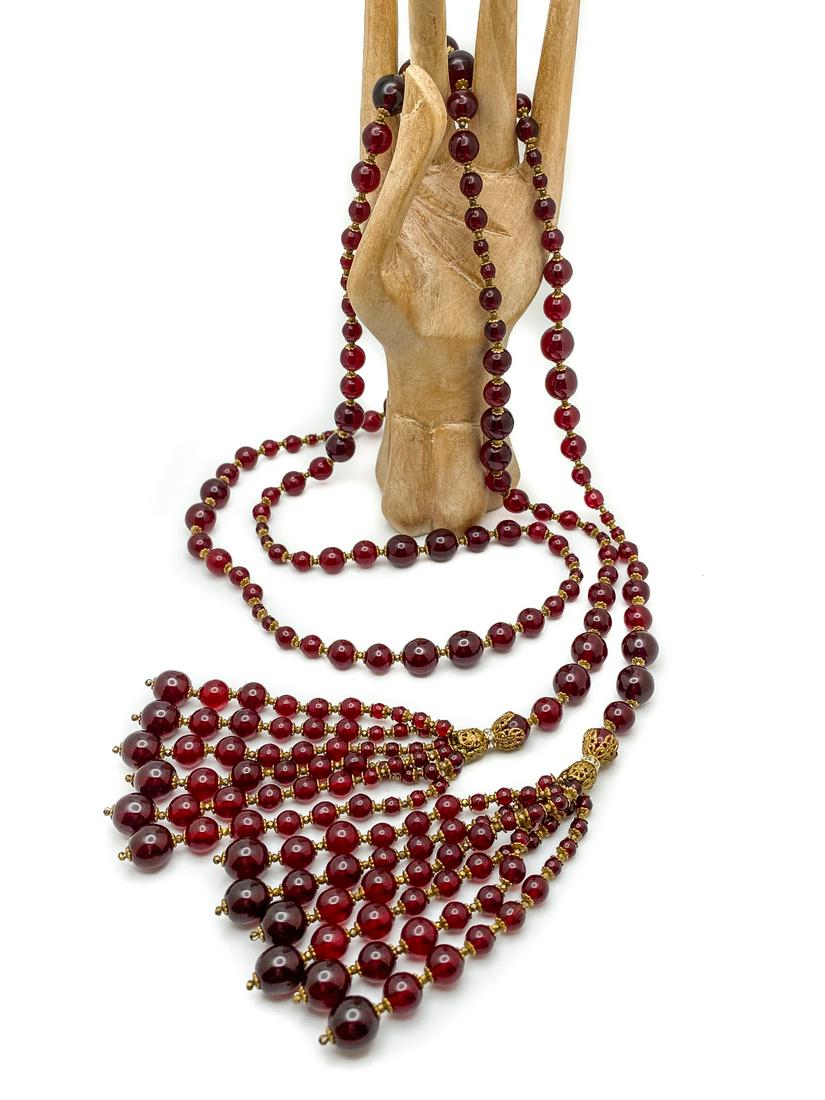 Beaded Open Tie Necklace.: Long strand of shiny burgundy round beads, spaced with cup-shaped gilt findings, in a graduate pattern. Ending with tassels of six strands of the same beads, connected with cup-shaped gilt findings an