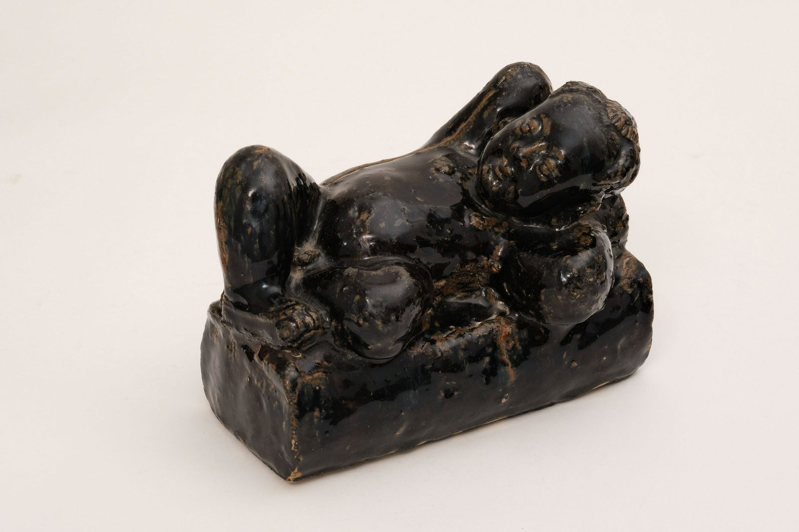 A Black -Glaze Child-Shape Pillow: A Black -Glaze Child-Shape Pillow. H: 6.7 in. (17 cm) W: 9.1 in. (23 cm) D: 4.3 in. (11 cm)