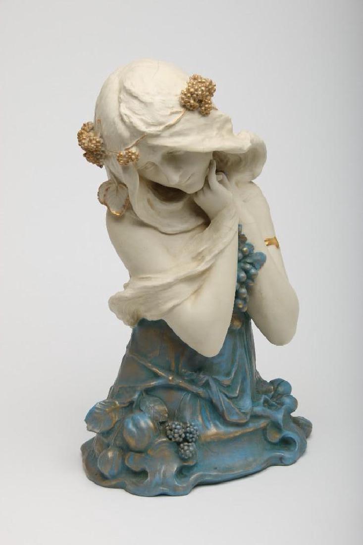 Art Nouveau Earthenware Portrait Bust Young Woman: Art Nouveau glazed earthenware portrait bust of a young woman wearing foliate crown with hands clasped around a bunch of grapes. Made in Austria. Measures 14" high.
