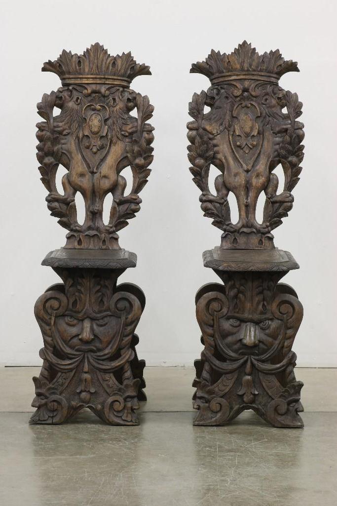Pair Gothic Spanish Revival Carved Wood Chairs: Lion and human face motif carved wood chairs. Each approx. 50 in H x 17 in W x 19 in D.