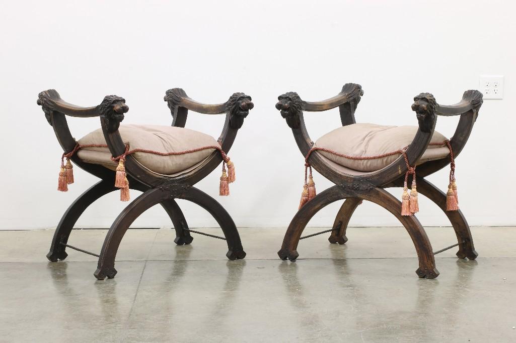 Pair 19th C. Gothic Spanish Revival Carved Walnut: Approx. 29 W x 29.75 D x 30.75 T. Pair of stately savonarola two-sided chairs with custom cushion with tassels. Heavily carved with lions heads on all corners and wrought iron stretchers.