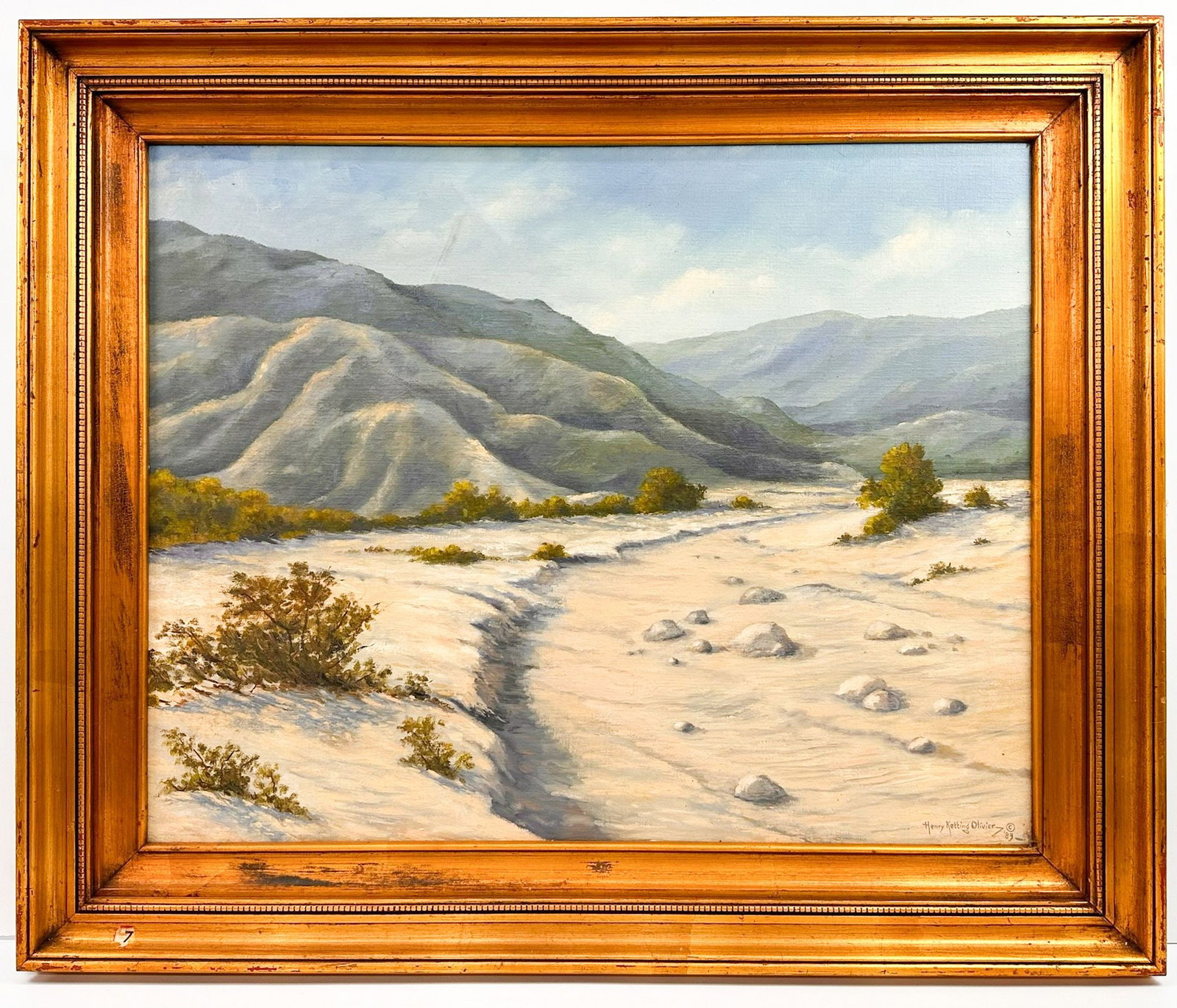 Henry Ketting Olivier (1924-2004) Oil on Canvas, Desert Wash, 1983: Oil on canvas titled "Desert Wash" signed and dated 1983. The painting depicts a desert landscape with mountains and a dry riverbed. Framed. Visible artwork is approximately 23.5 in H x