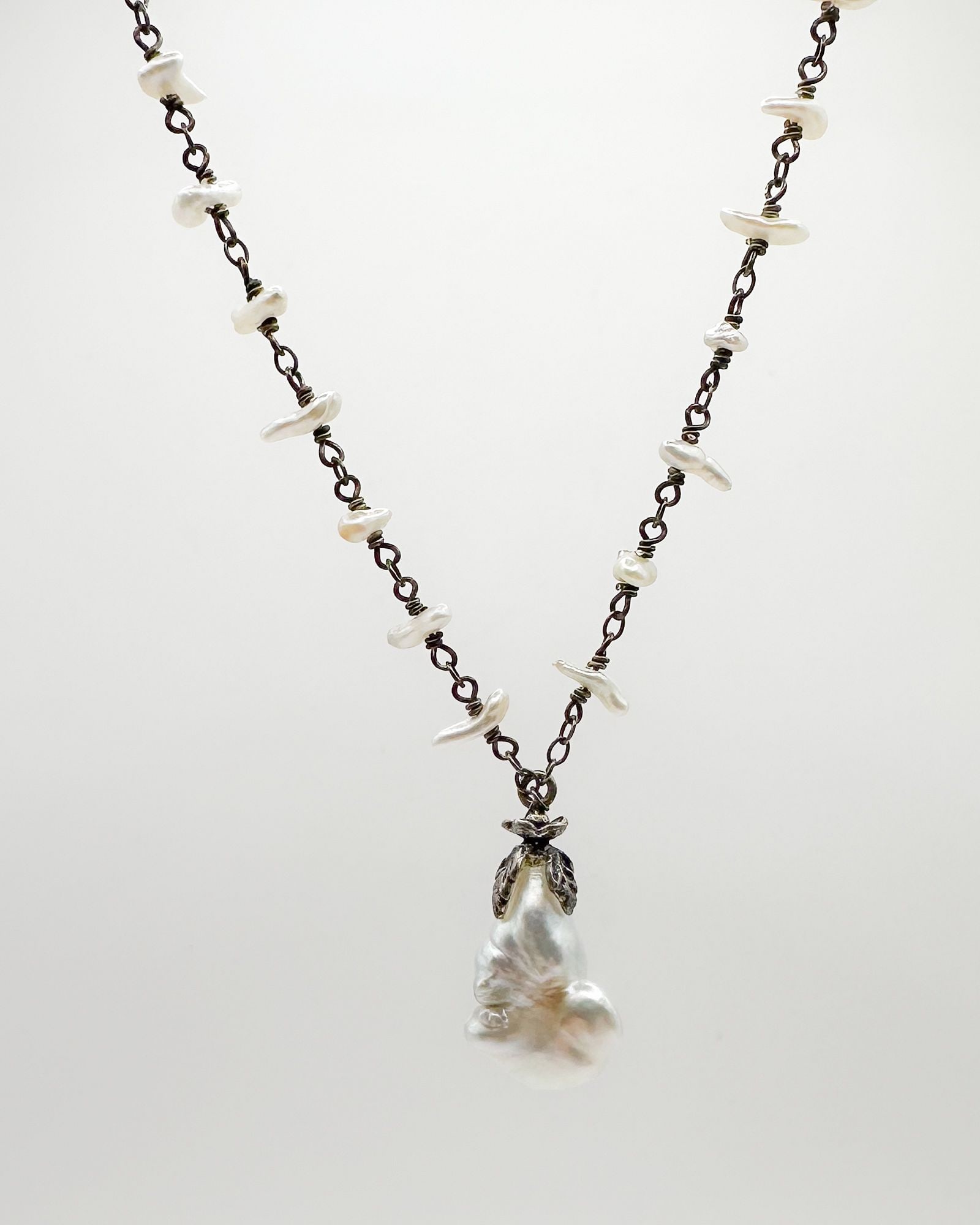 Sage Machado Baroque Pearl Pendant Necklace: Sage Machado necklace featuring baroque pearl pendant with floral clasp. Designer signed. Chain interspersed with small pearls. Measures 16 inches in length.