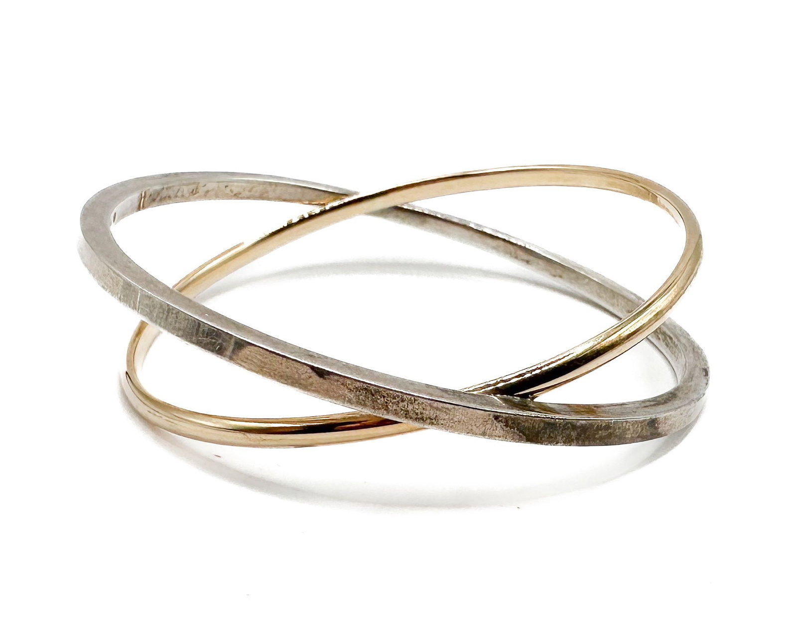 The Golden Bear Sterling Silver and 14K Yellow Gold Interlocking Bangle Bracelet: Two-tone bangle bracelet featuring interlocking sterling silver and 14K yellow gold bands. Interior circumference measures approximately 7 inches. Combined weight: 31.3 grams.