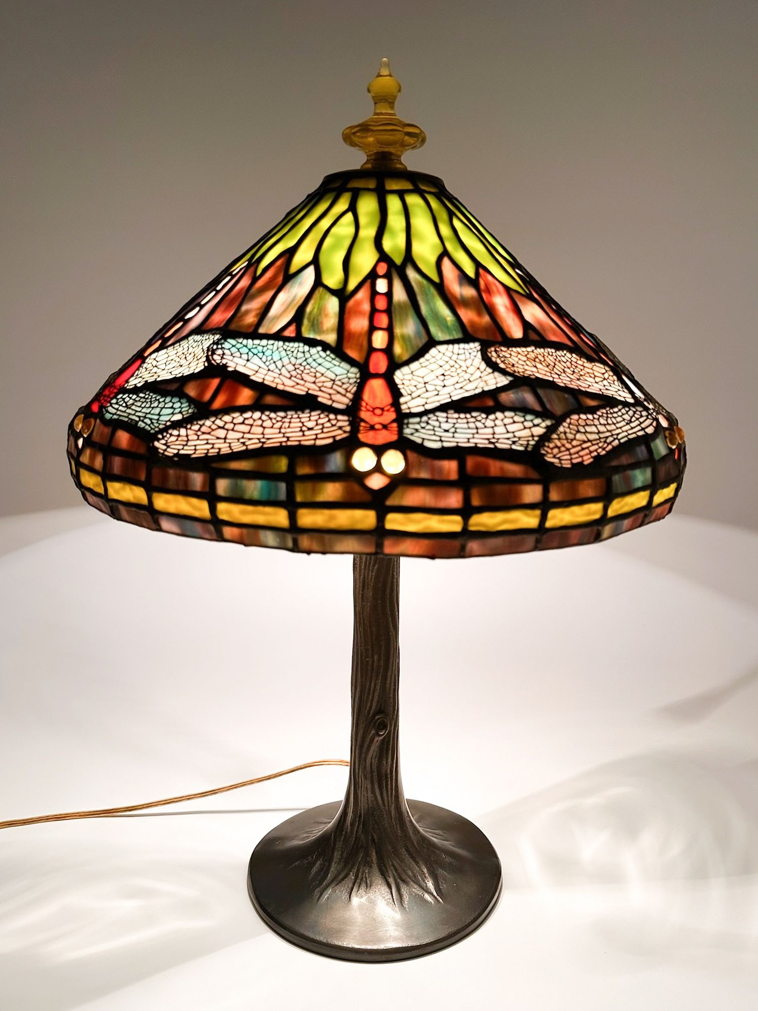 Tiffany Style Stained Glass Dragonfly Table Lamp: Older copy of a Tiffany dragonfly lamp. Stained glass lampshade and metal base. Lamp features dragonflies with iridescent wings. Approximately 24 in H x 16 in W x 16 in D. Weighs approximately 12 lbs 