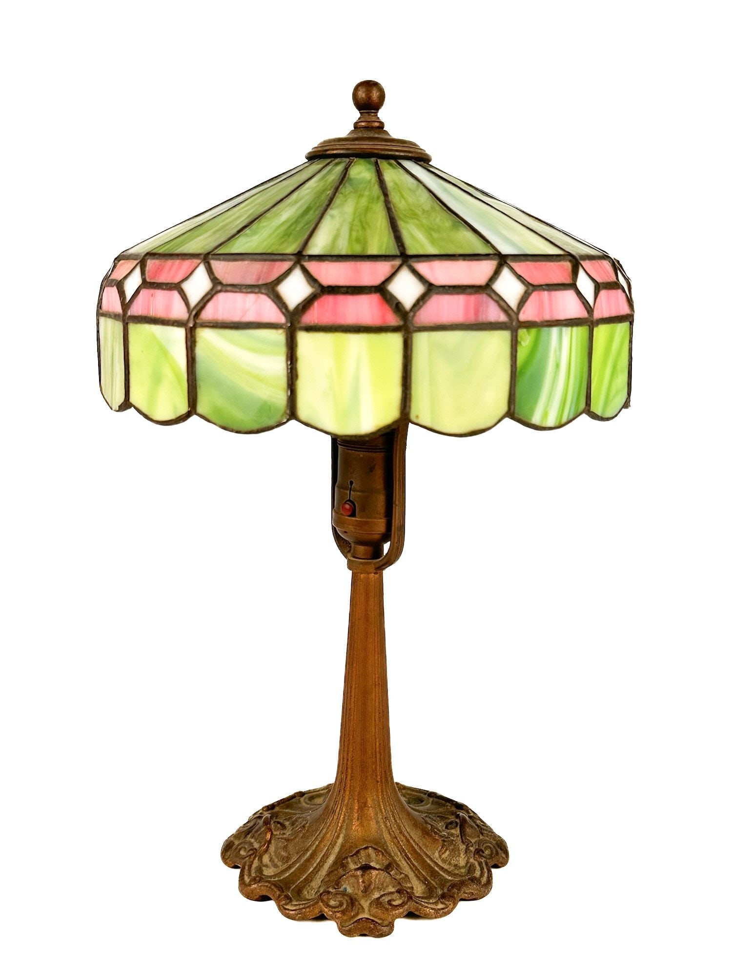 Antique B.B. Co. Stained Glass Table Lamp: Metal base with stained glass shade. Stained glass made of geometric shapes in shades of green, pink, and white. Base has B.B. Co. in the metal mold. Approximately 15 in H x 9.5 in W x 9.5 in D. Weigh