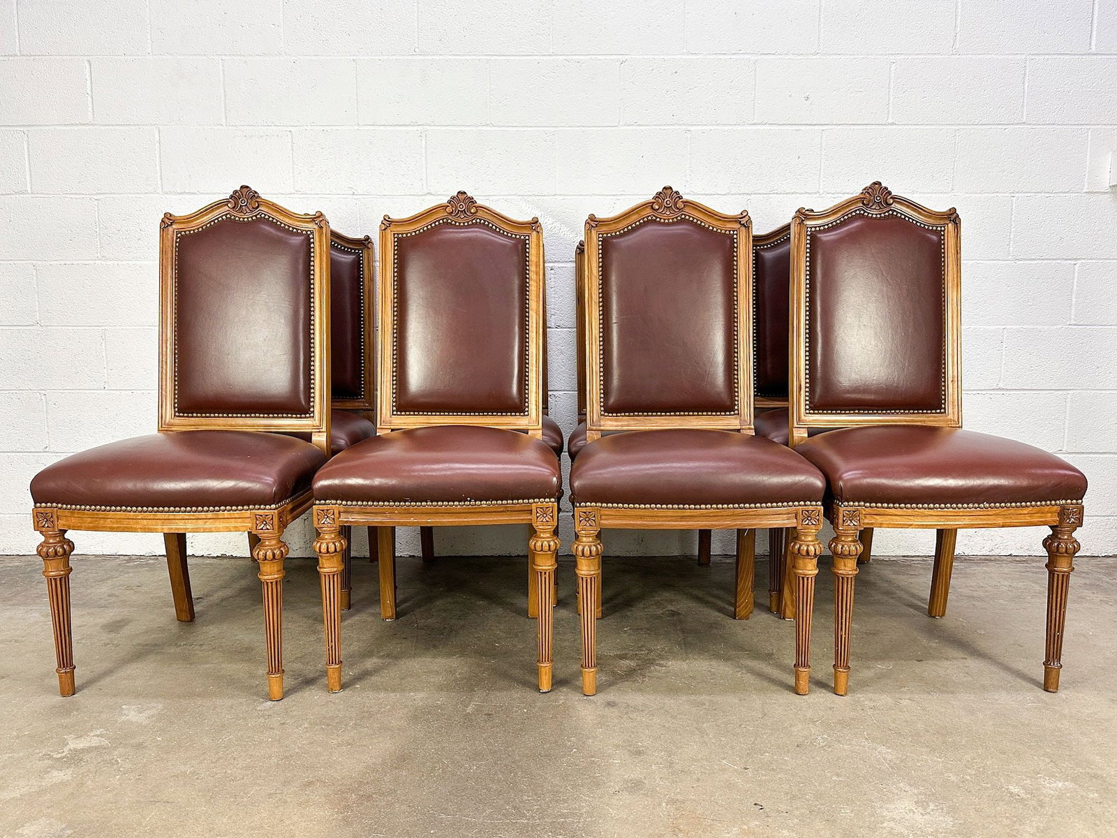 Set Of 8 Contemporary Walnut And Faux Leather Dining Chairs: Set of 8 dining chairs with riveted faux leather upholstery and walnut wood construction. Fluted legs. Nice carved wood accent on backrest. Dimensions: Each chair is approx. 43.25 in H x 20 in W x 20 