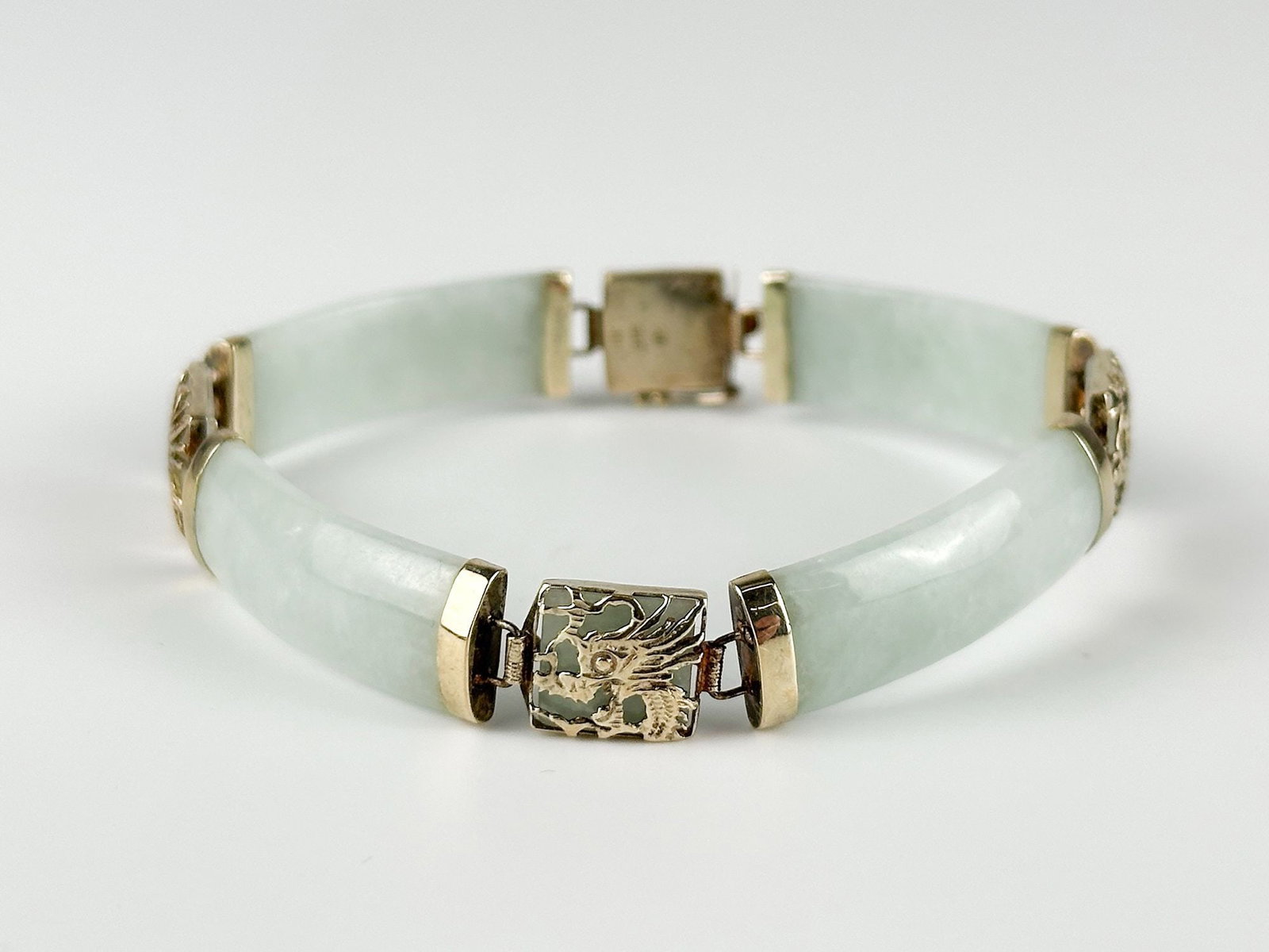 Green Jade and 14K Gold Dragon Panel Bracelet: Bracelet features Chinese style dragon cut outs in gold over slabs of jade panel. Stamped HK 585. Approximately 0.5 in H x 7.5 in W. Weighs approximately 16.4 grams. LOCAL PICK UP INFORMATION: Wednesd