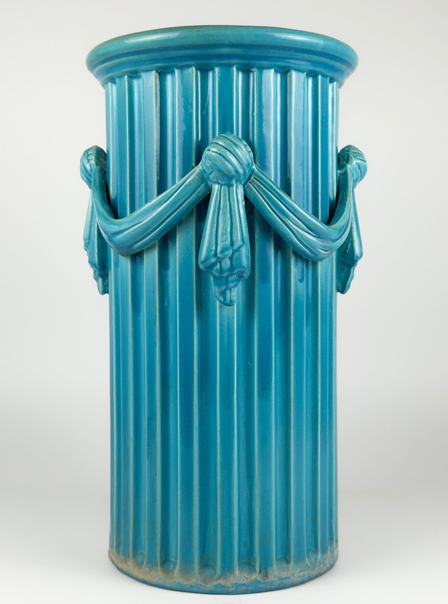 Burmantofts-Style Turquoise Glazed Pottery Jardiniere with Draped Swags: Turquoise glaze. Neoclassical fluted column design accented with draped swags and knots. Approximately 19.5 in H x 11 in W x 11 in D. Weighs approximately 13 lbs 11 oz. LOCAL PICK UP INFORMATION: Wedn
