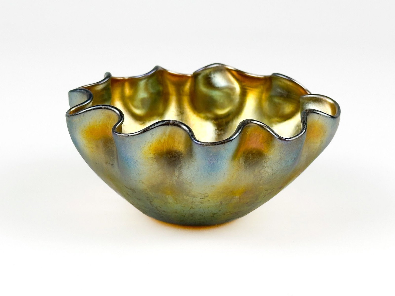 Louis Comfort Tiffany Iridescent Glass Bowl, Marked LCT: Louis Comfort Tiffany Favrile glass iridescent bowl with a freeform ruffled rim and luminous surface exhibiting orange, gold, and subtle blue-green tones. The interior and exterior feature a rich irid