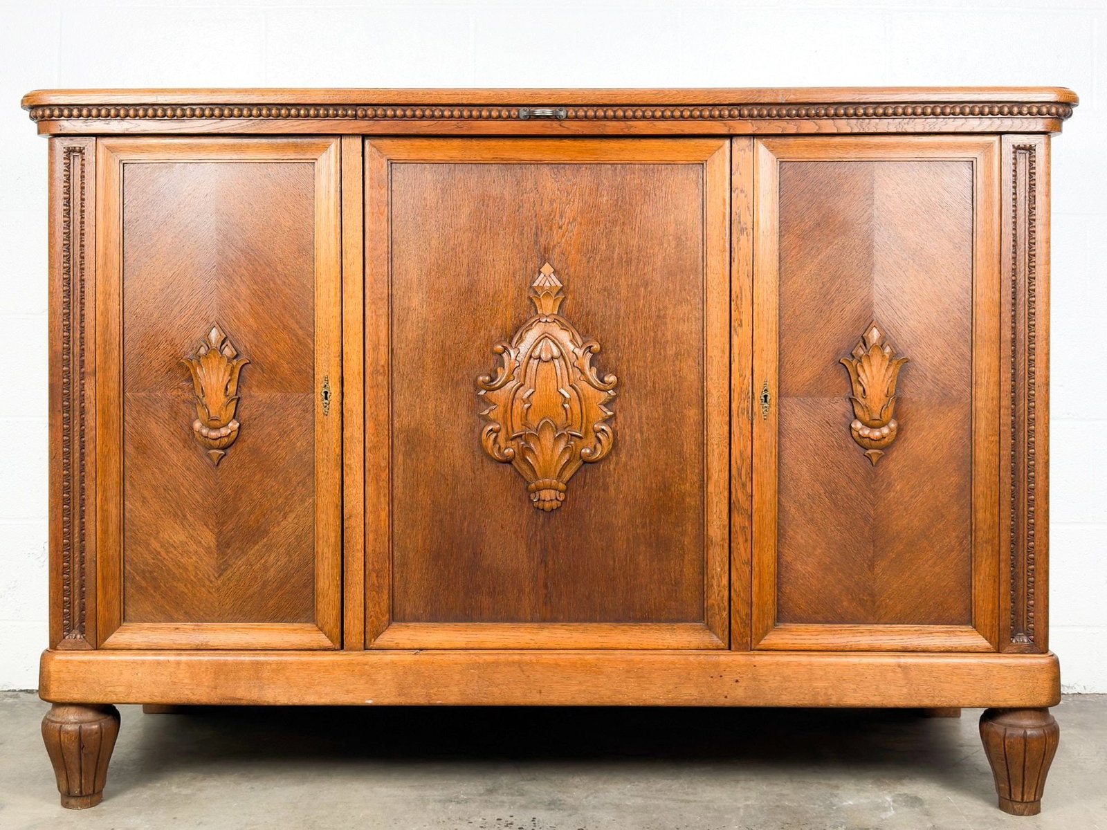 French Art Deco Carved Oak Three-Door Buffet Sideboard: Antique style sideboard made of carved wood with book-matched panels, beaded edge and carved foliate cartouches. Wood tray that slides out along top. Three doors with two compartments and shelving ins