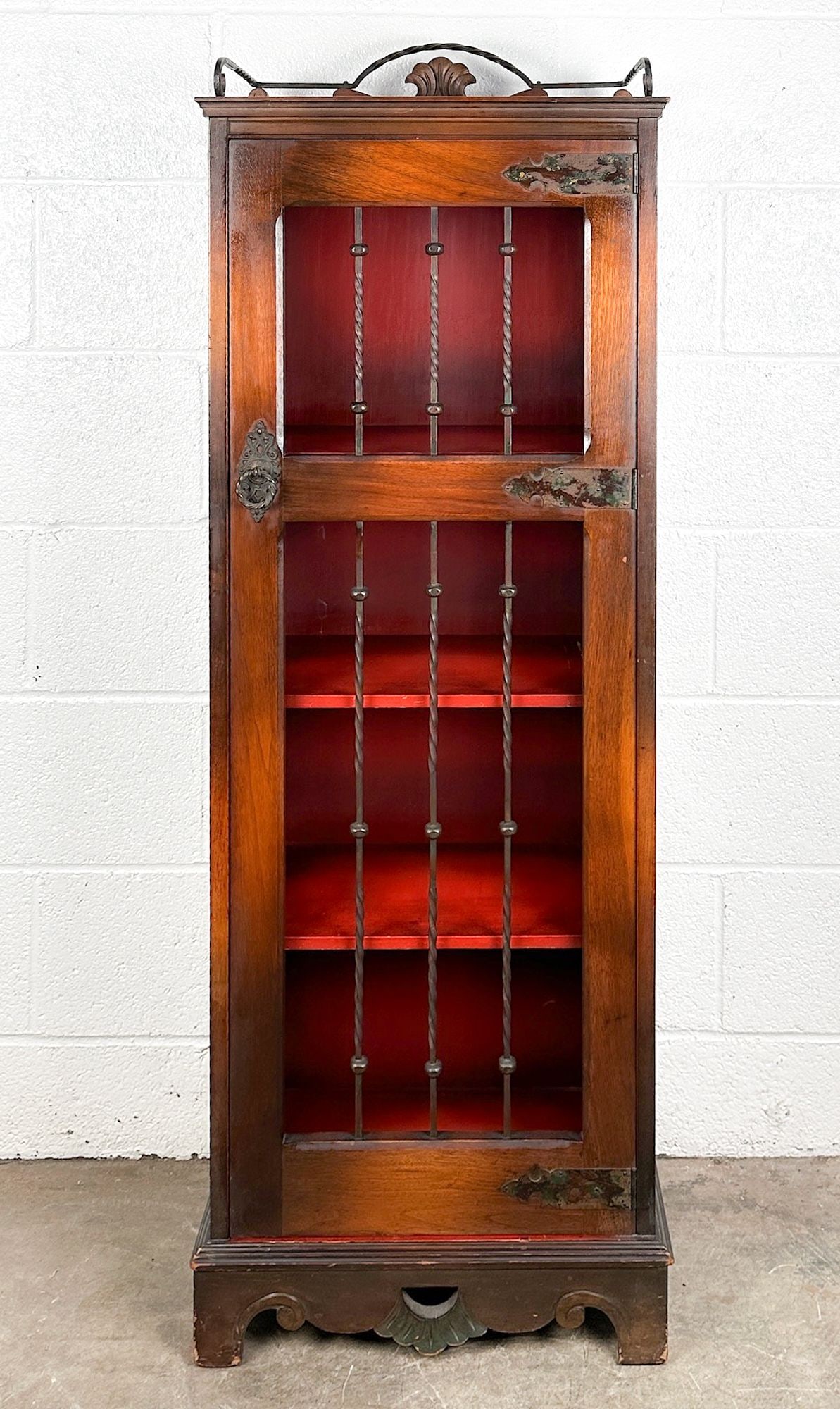 Spanish Revival Narrow Display Cabinet with Barred Iron-Spindle Door: Twisted wrought iron accents on door and top shelf. Cherry red and black painted interior. 4 shelves. Dimensions: Bookshelf is approx. 51.5 in H x 18 in W x 10.5 in D. LOCAL PICK UP INFORMATION: Wedne