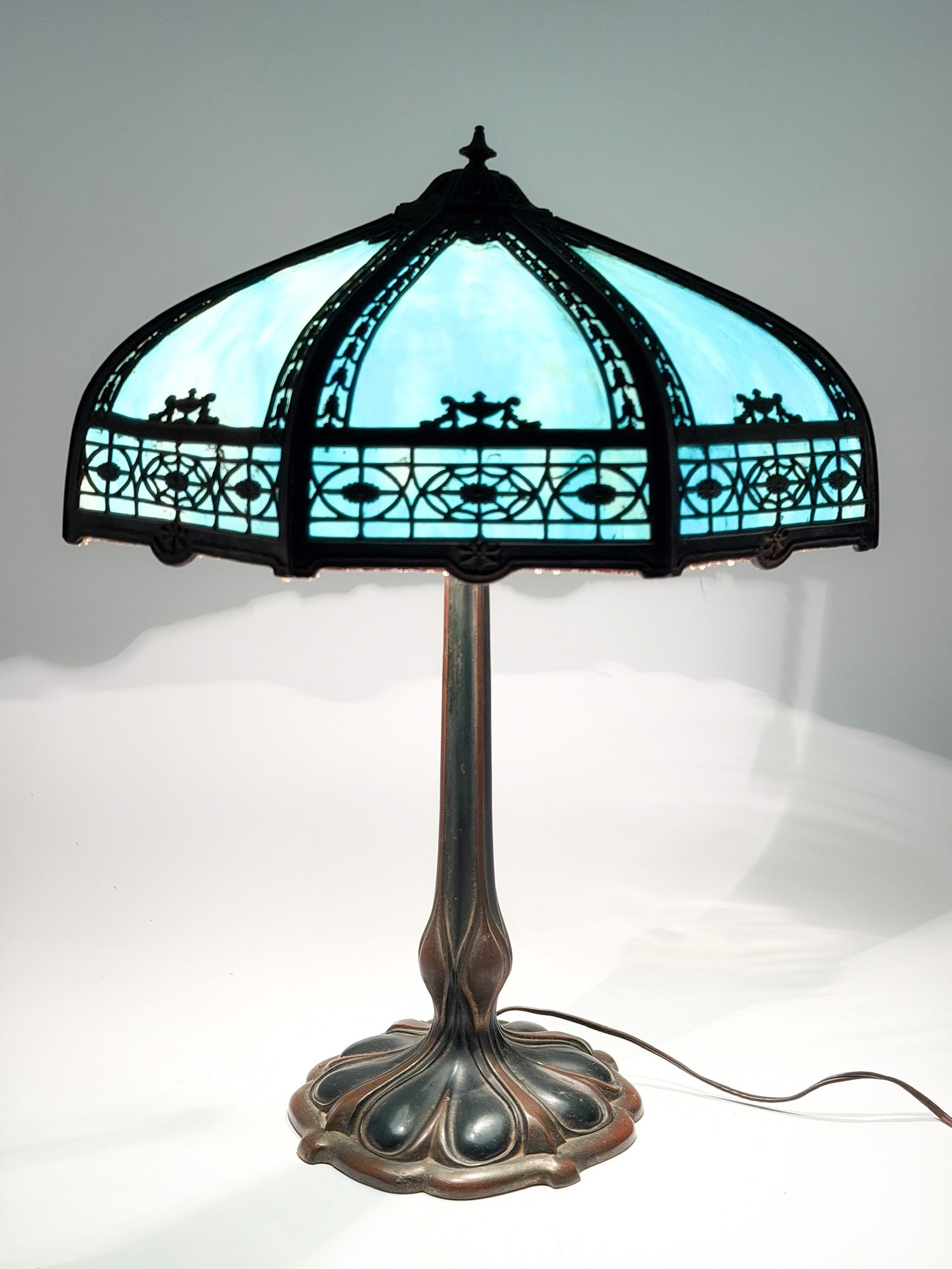 Antique Slag Glass Panel Lamp with Filigree Overlay on Art Nouveau Cast Base: Blue slag glass behind a pierced filigree overlay cast with classical urns, swags, and scrollwork, on an Art Nouveau cast-metal standard with a foliate organic-form base, American, circa 1915-192