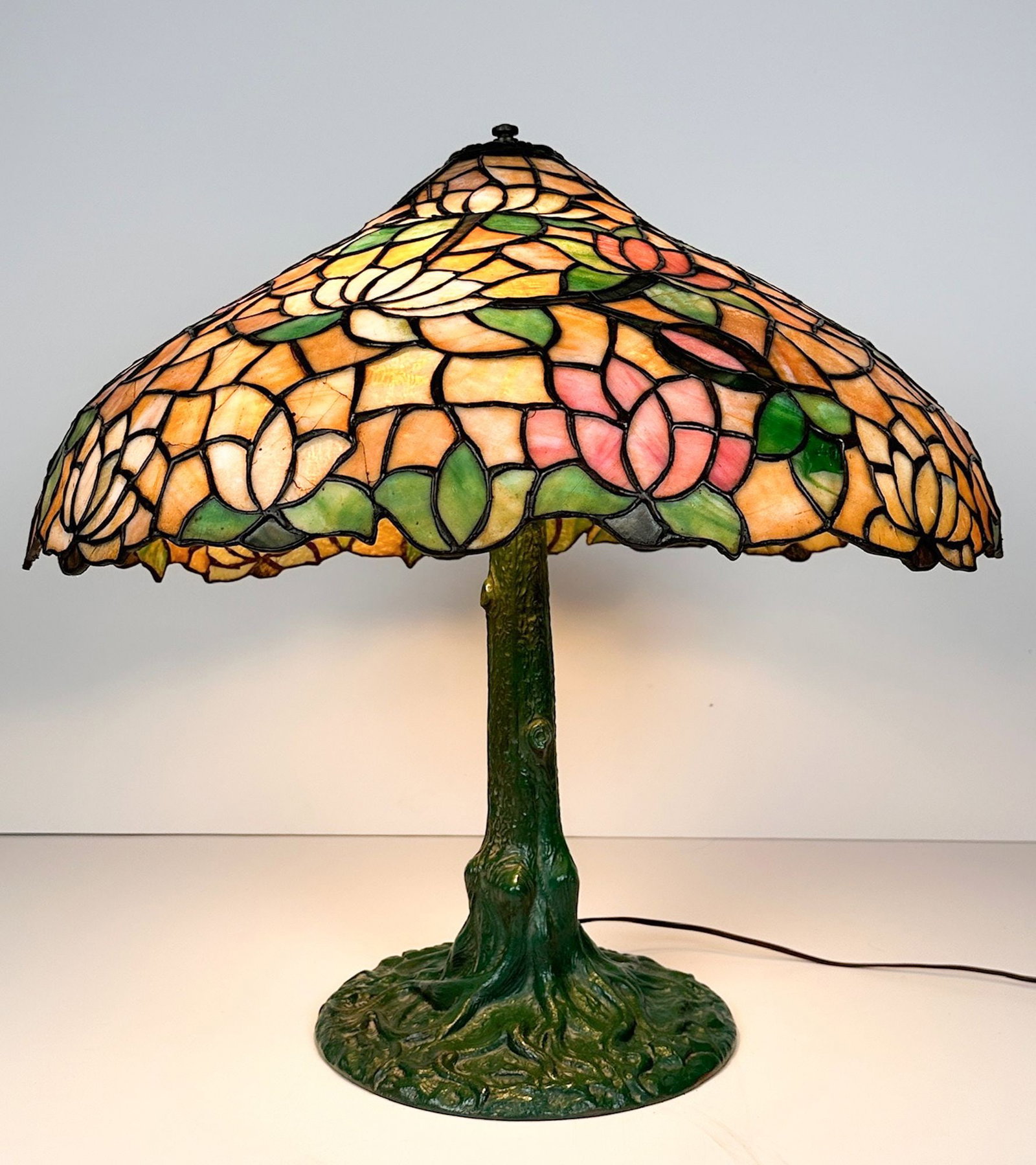 Tiffany Style Stained Glass Table Lamp with Floral Motif: Tree trunk base motif. Lily floral design. 3 bulbs. Dimensions: Lamp is approx. 24 in H x 24.5 in dia. Weighs 30 lbs. LOCAL PICK UP INFORMATION: Wednesday, July 8, 10:00 AM - 2:00 PM 8059 Foothill Blv