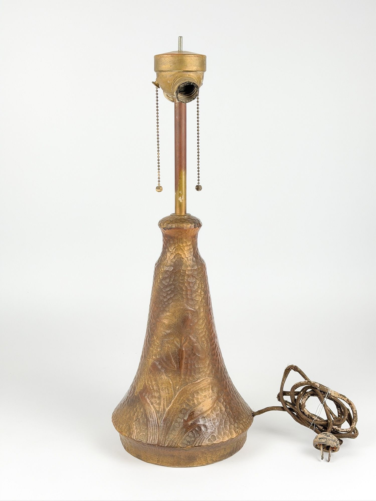 Arts & Crafts Pottery Lamp Base with Hammered-Texture Bronze Glaze: Base is made of cast ceramic in shades of copper and earth. Depicts a blooming iris on either side with pebbled background. Approximately 21.5 in H x 8 in W x 8 in D. Weighs approximately 7 lbs 12 oz.