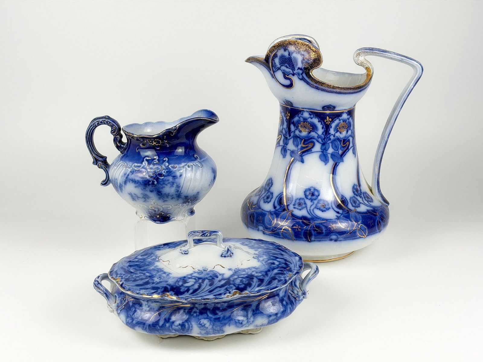 Lot of 3 Flow Blue with Gilt, Floral Pitcher, Covered Vegetable Dish and Cream Jug: Large Floral Ewer/Pitcher, Myott Etruscan Covered Vegetable Dish, and Embossed Cream Jug. Pieces depict floral motifs with gold painted embellishments. Sizes vary from approximately 5 in H x 11.5 in W