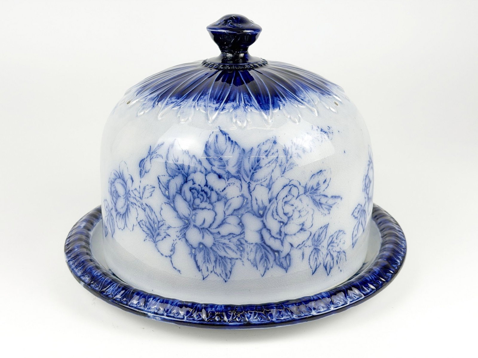 Antique Staffordshire Flow Blue Ironstone Lidded Cheese Dome with Floral Motifs: Two piece set features a plate and handled cover with floral motifs throughout. Approximately 8.5 in H x 11.75 in W x 11.75 in D. Weighs approximately 4 lbs 13 oz. LOCAL PICK UP INFORMATION: Wednesday