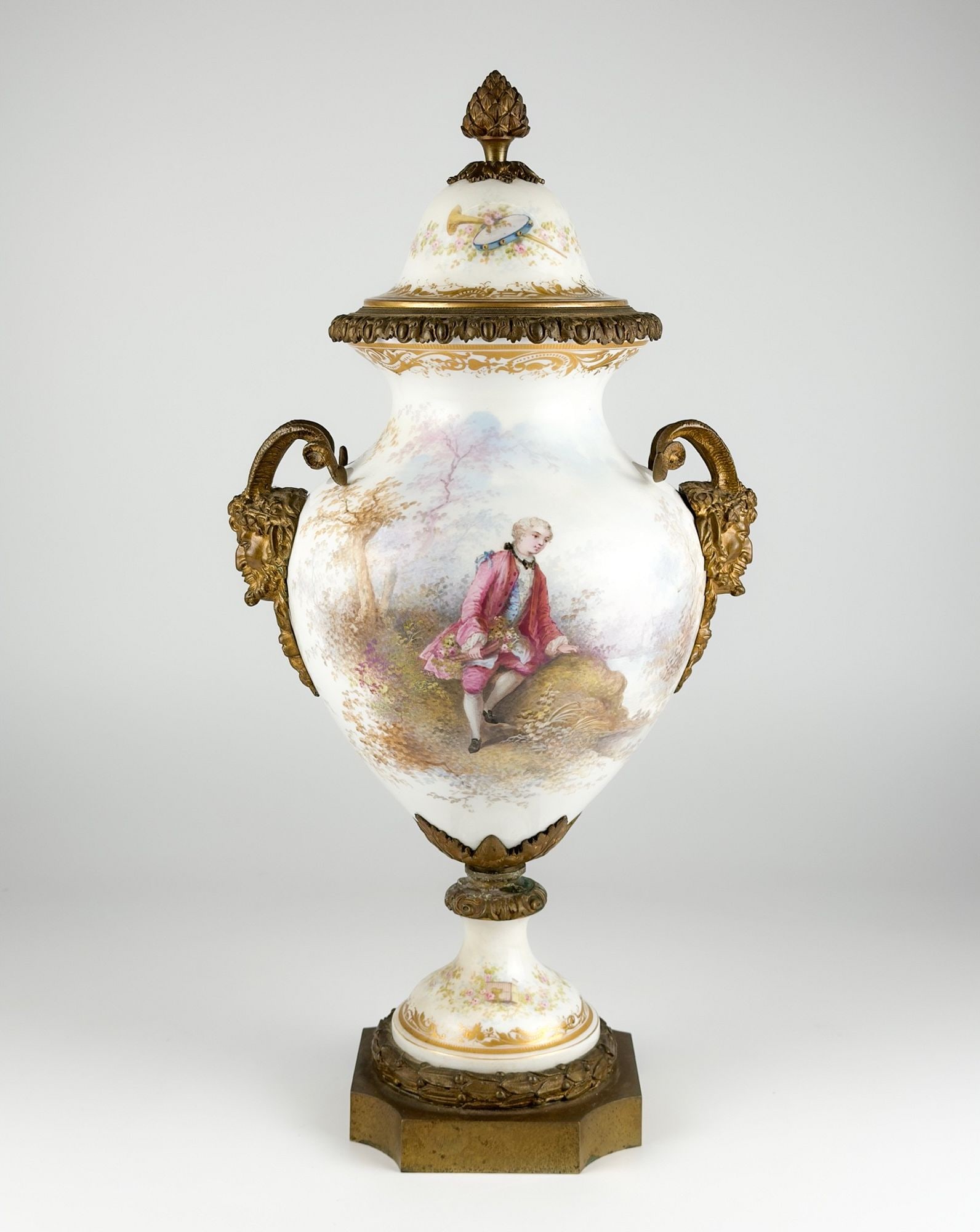 SÃ¨vres-Style Porcelain and Gilt-Bronze Mounted Covered Urn: Features bronze base and hardware. Depicts daily scenes of people in nature with floral and faun handled bronze motifs, as well as gilded gold details. Approximately 20.5 in H x 10.25 in W x 8 in D. W