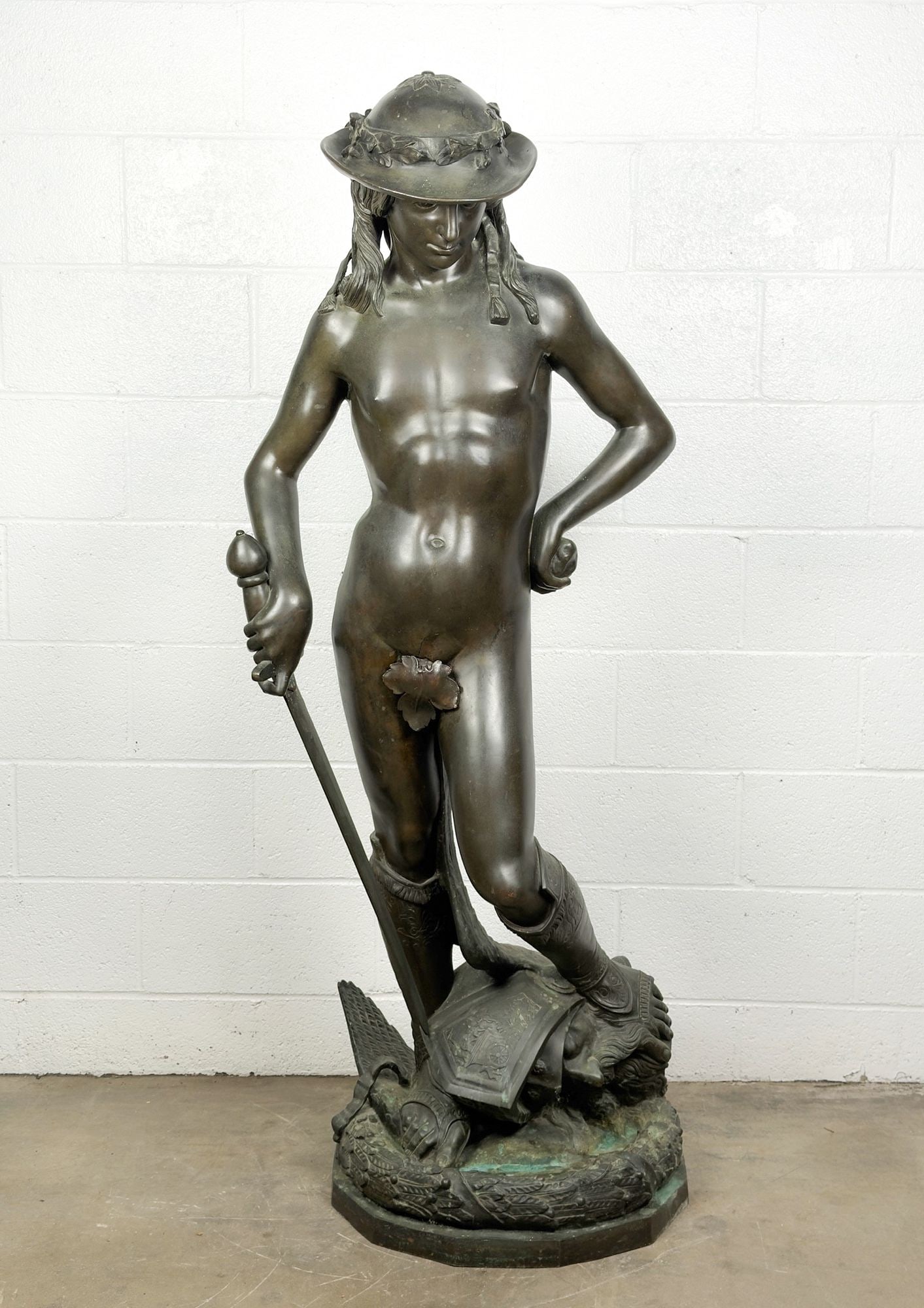 After Donatello, Bronze Sculpture, David and Goliath, Mid 20th Century: Titled David and Goliath. Unsigned. Depicts a scene from the biblical tale of David standing contrapposto with a stone in his left hand, a sword in his right, and a foot on top of Goliath's severed he