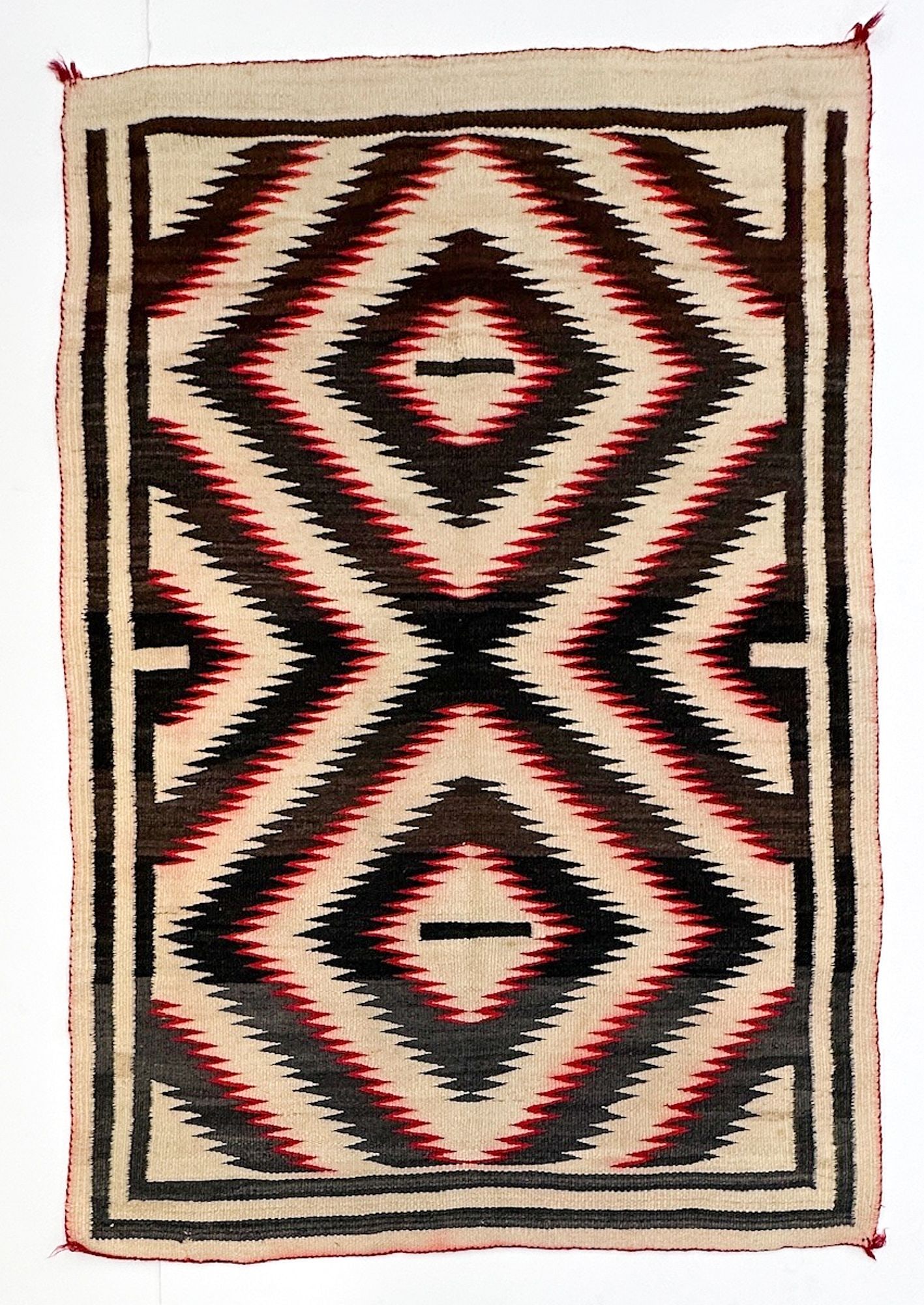 Navajo Ganado Regional Wool Rug, Serrated Diamond Design: Geometric red, brown, beige and gray design. Red wool corner tassels. First half 20th century. Dimensions: Rug is approx. 68.25 in H x 47 in W. Weighs 7 lbs 9 oz. LOCAL PICK UP INFORMATION: Wednesday,